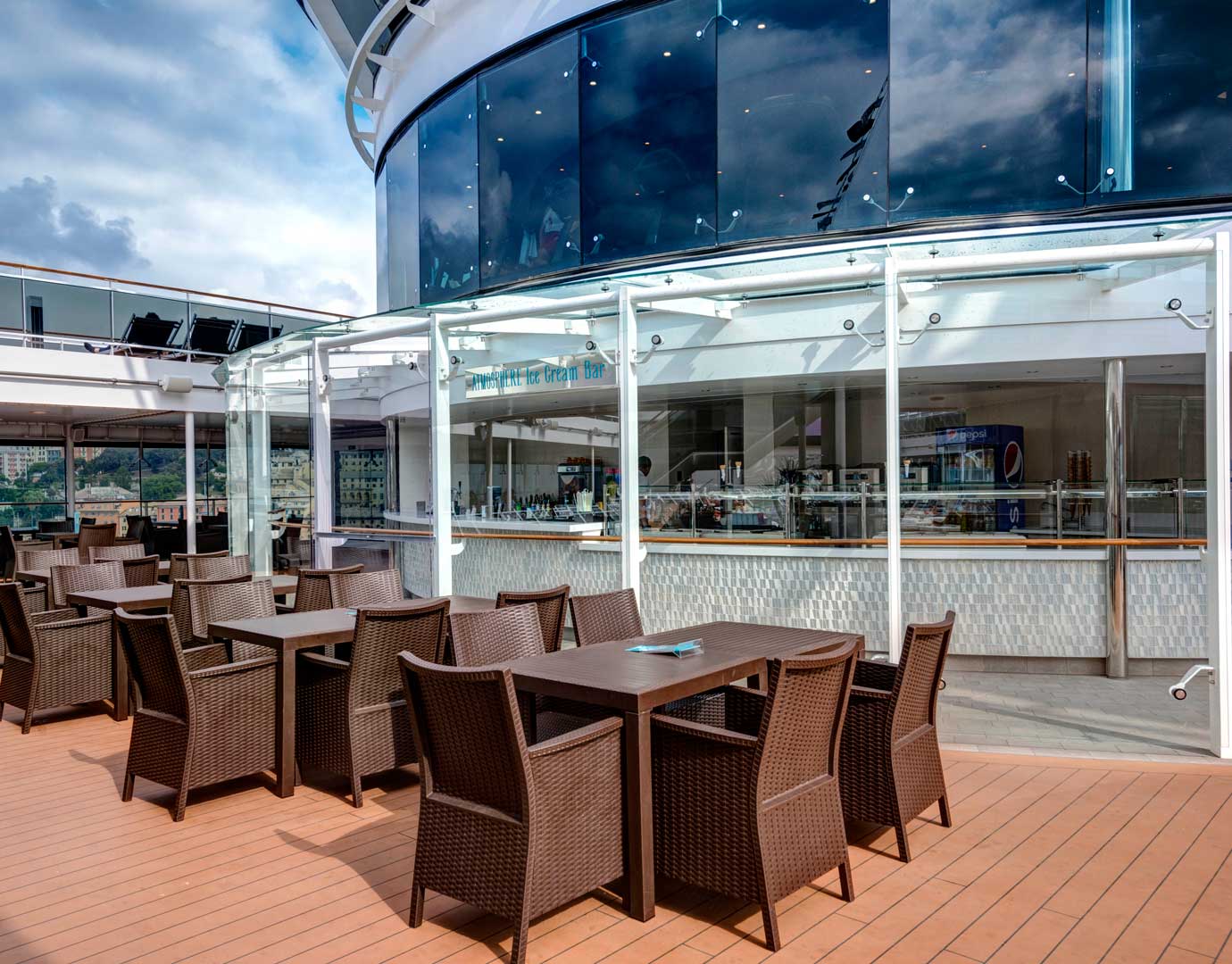 Outdoor dining area with wicker chairs and tables near an ice cream bar on an MSC cruise ship | MSC Cruises