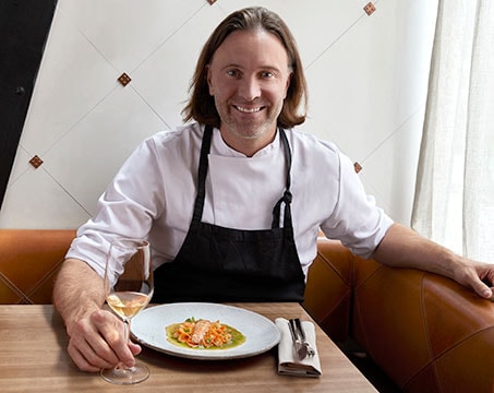A chef presenting a gourmet seafood dish with a glass of white wine in an elegant dining setting | MSC Cruises