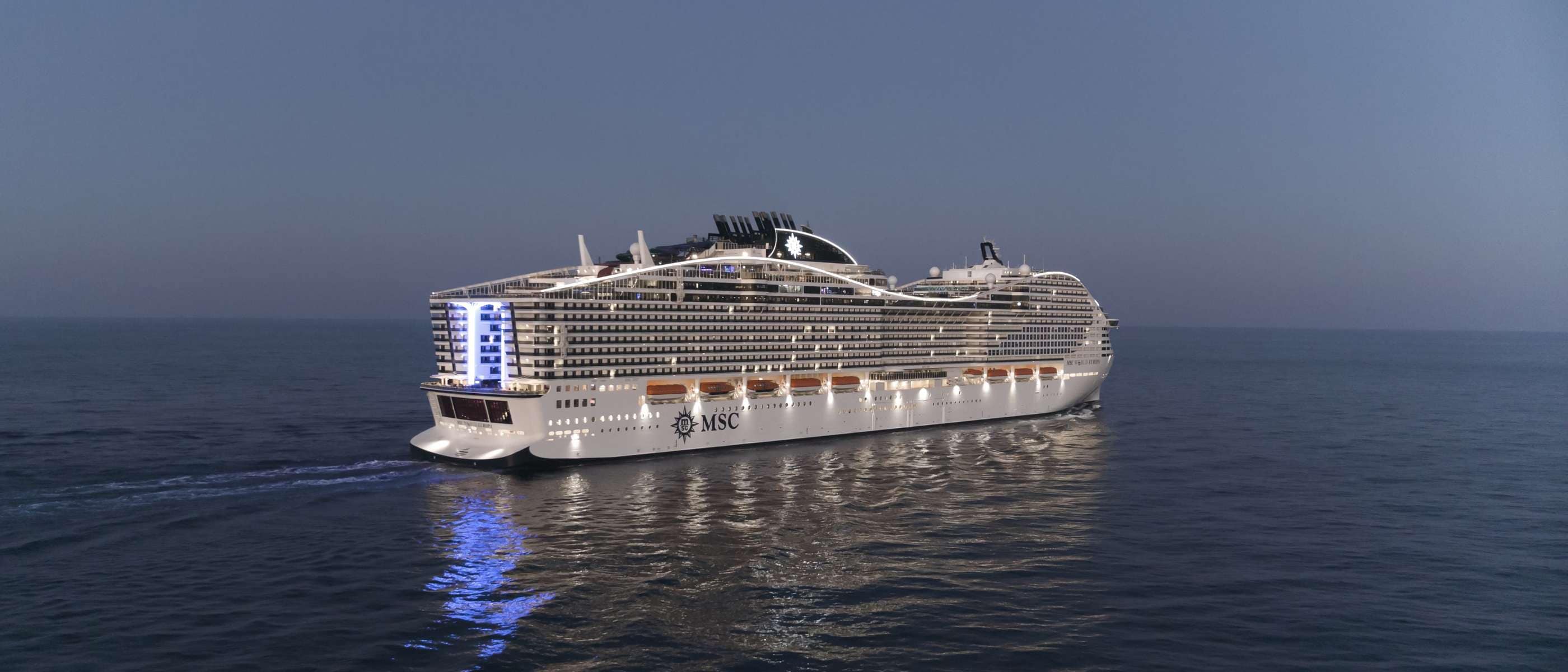An illuminated MSC cruise ship sailing on calm waters at dusk | MSC Cruises