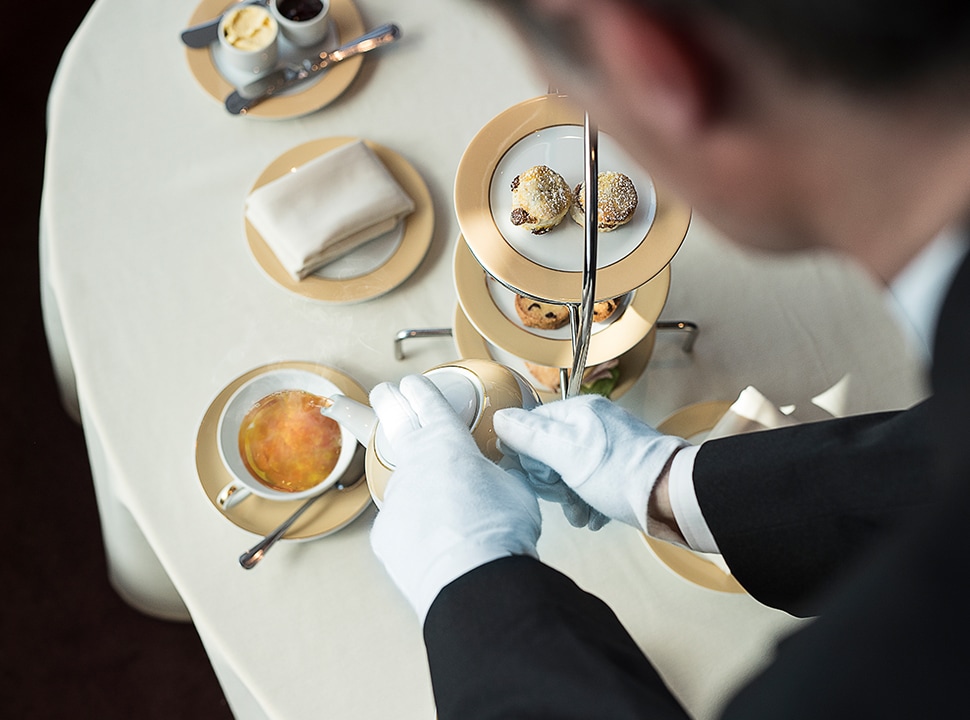A MSC Yacht 幸运飞船168综合开奖网站 butler in white gloves serves cruises guests tea and coffee with delicious pastries on a tiered.