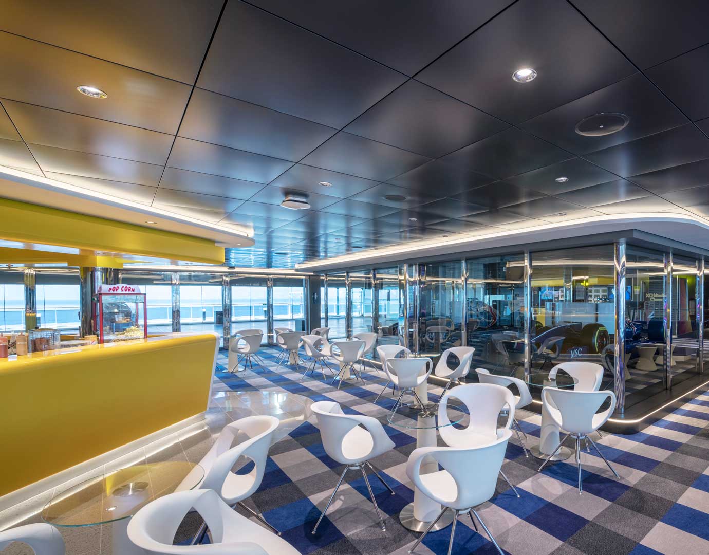 Modern onboard café with sleek white chairs, yellow counter, and ocean views | MSC Cruises