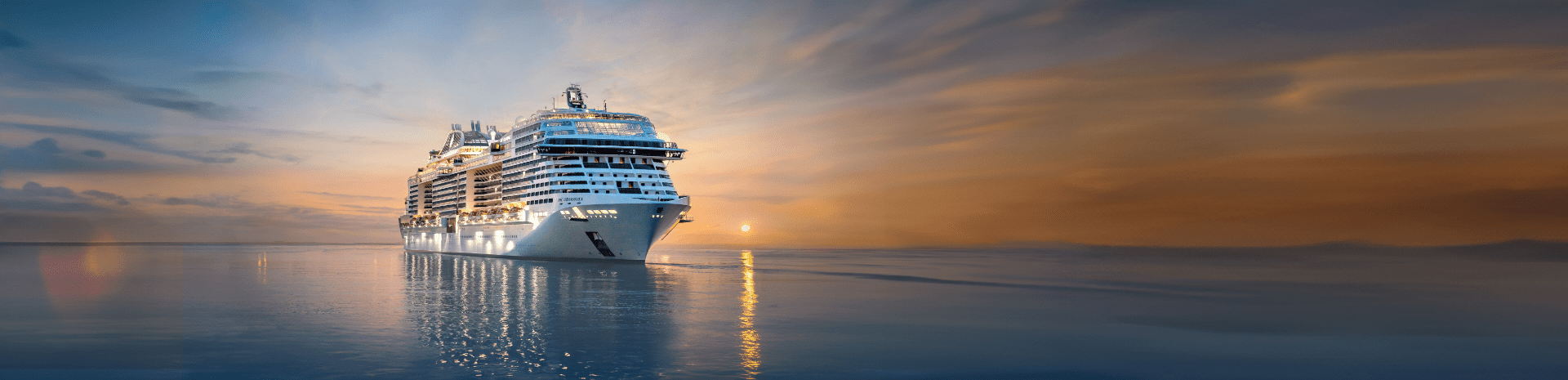 MSC Cruises ship MSC Grandiosa sailing on the open ocean with a setting sun in the background.