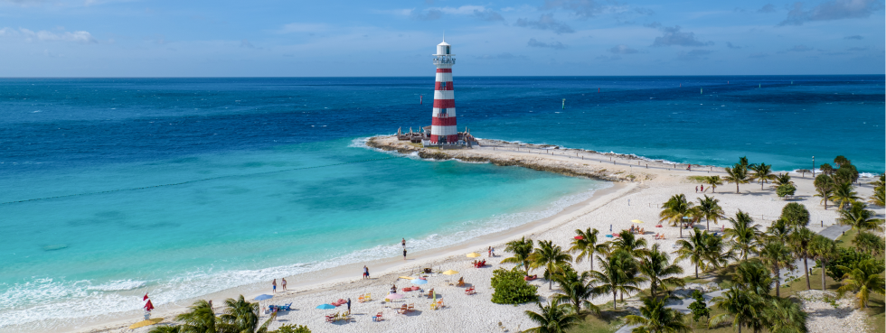 A panoramic view of a sprawling beach with guests paddle boarding in the clear blue water, complemented by the presence of a magnificent cruise ship elegantly positioned on the horizon.